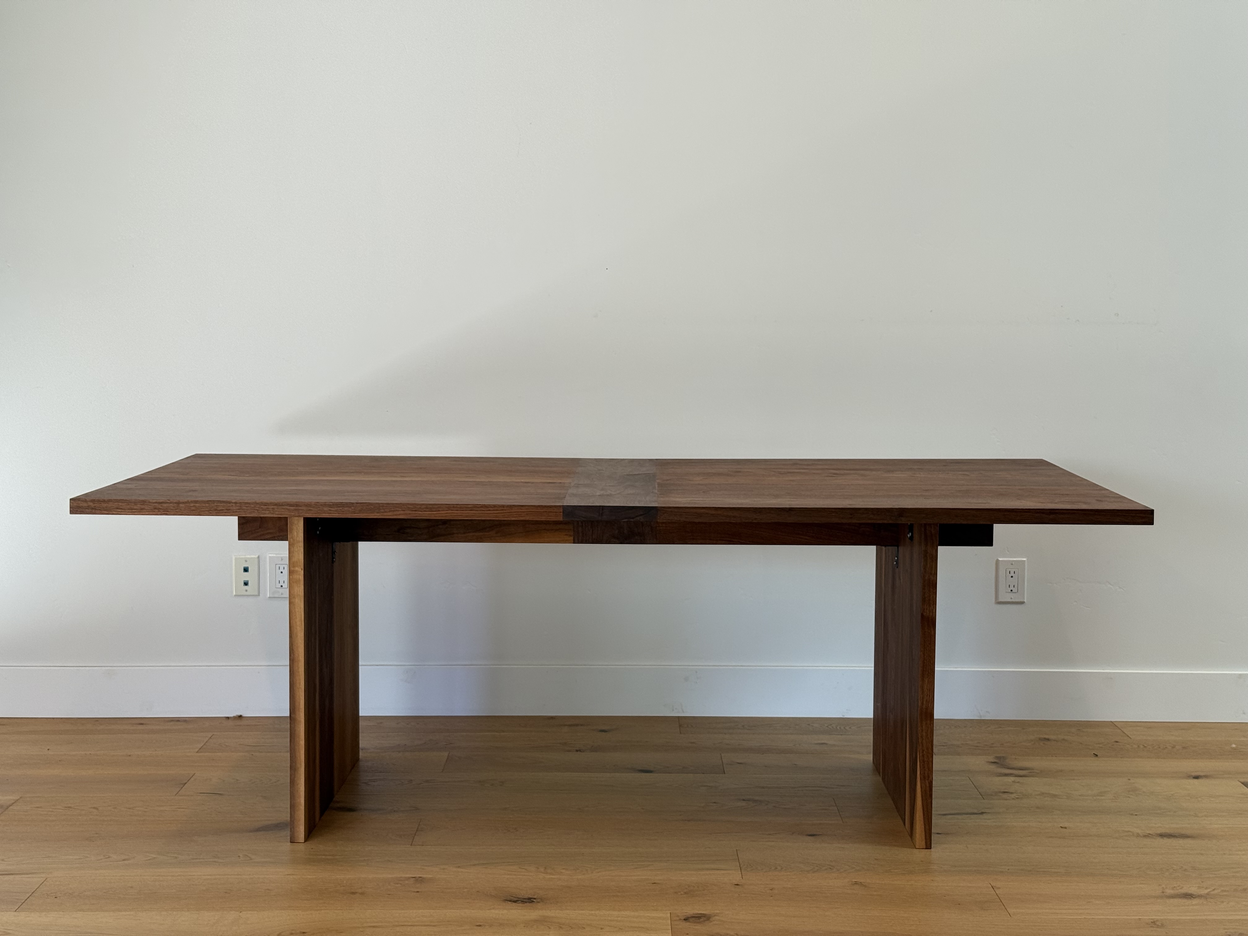 Walnut dining table, front view, against a white wall