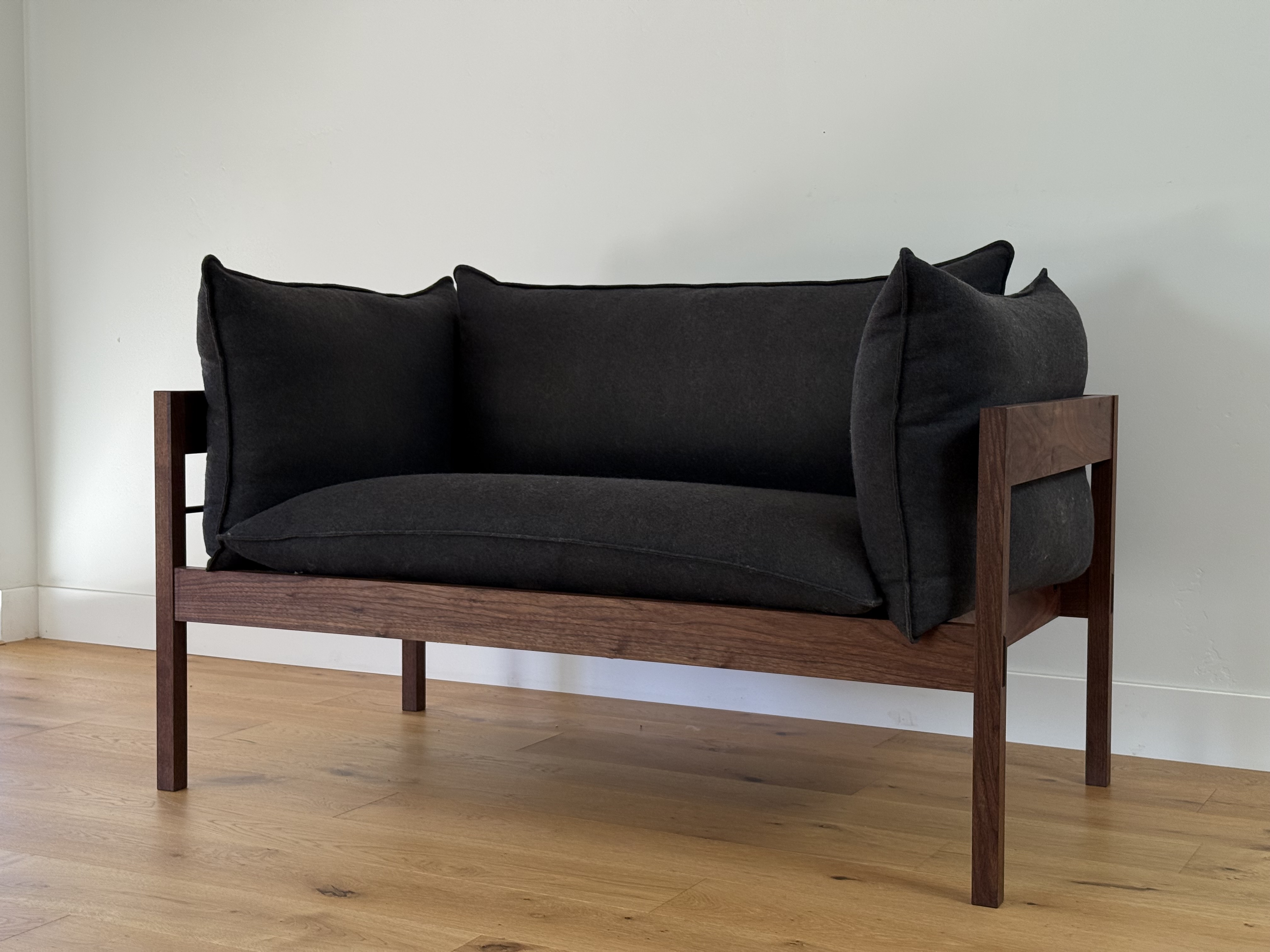 Walnut-framed loveseat, angled view with charcoal cushions
