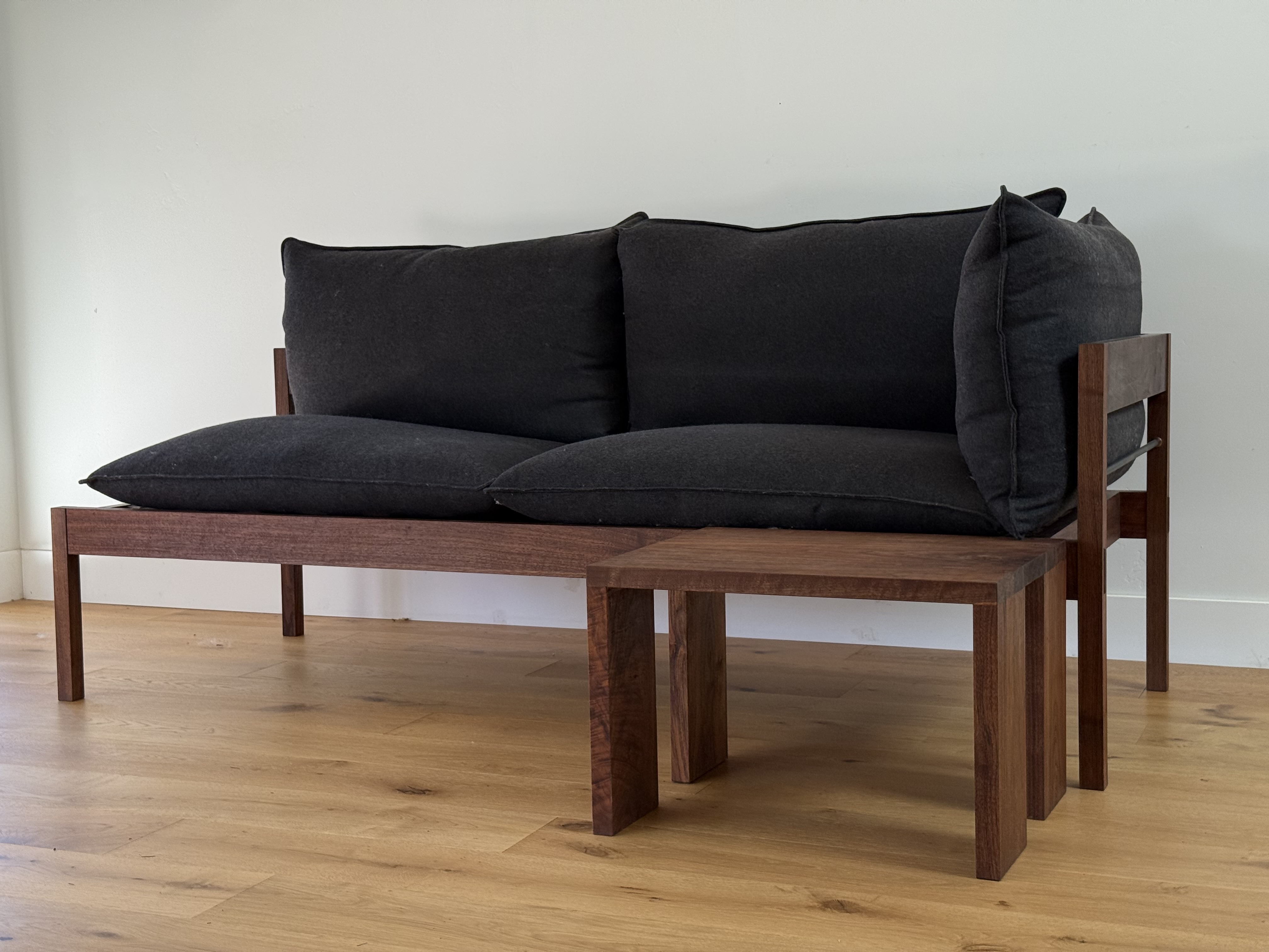 Walnut-framed sofa with charcoal cushions and matching side table, angled view